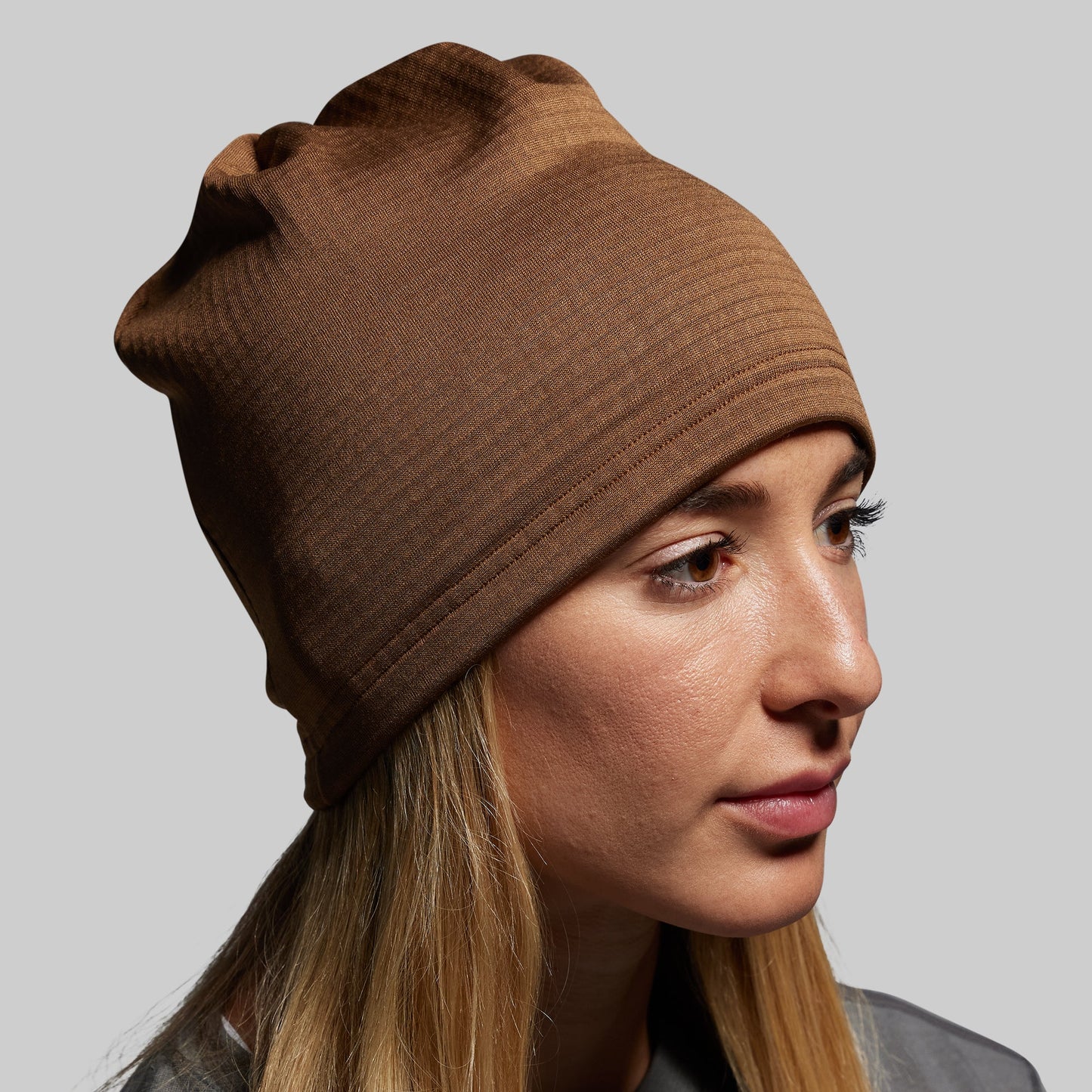 Woman wearing a brown beanie against a plain background