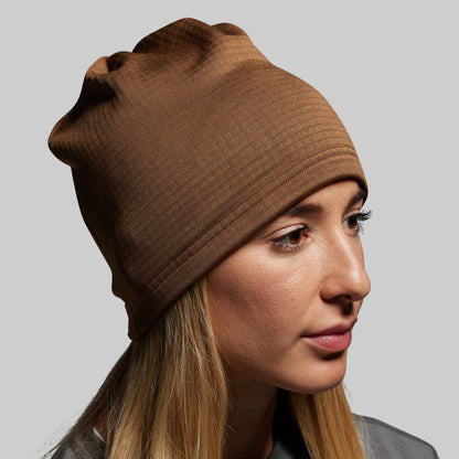 Woman wearing a brown beanie against a plain background