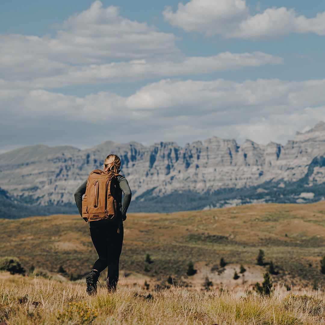 Woman in valley with mountain in the background wearing outdoor gear.