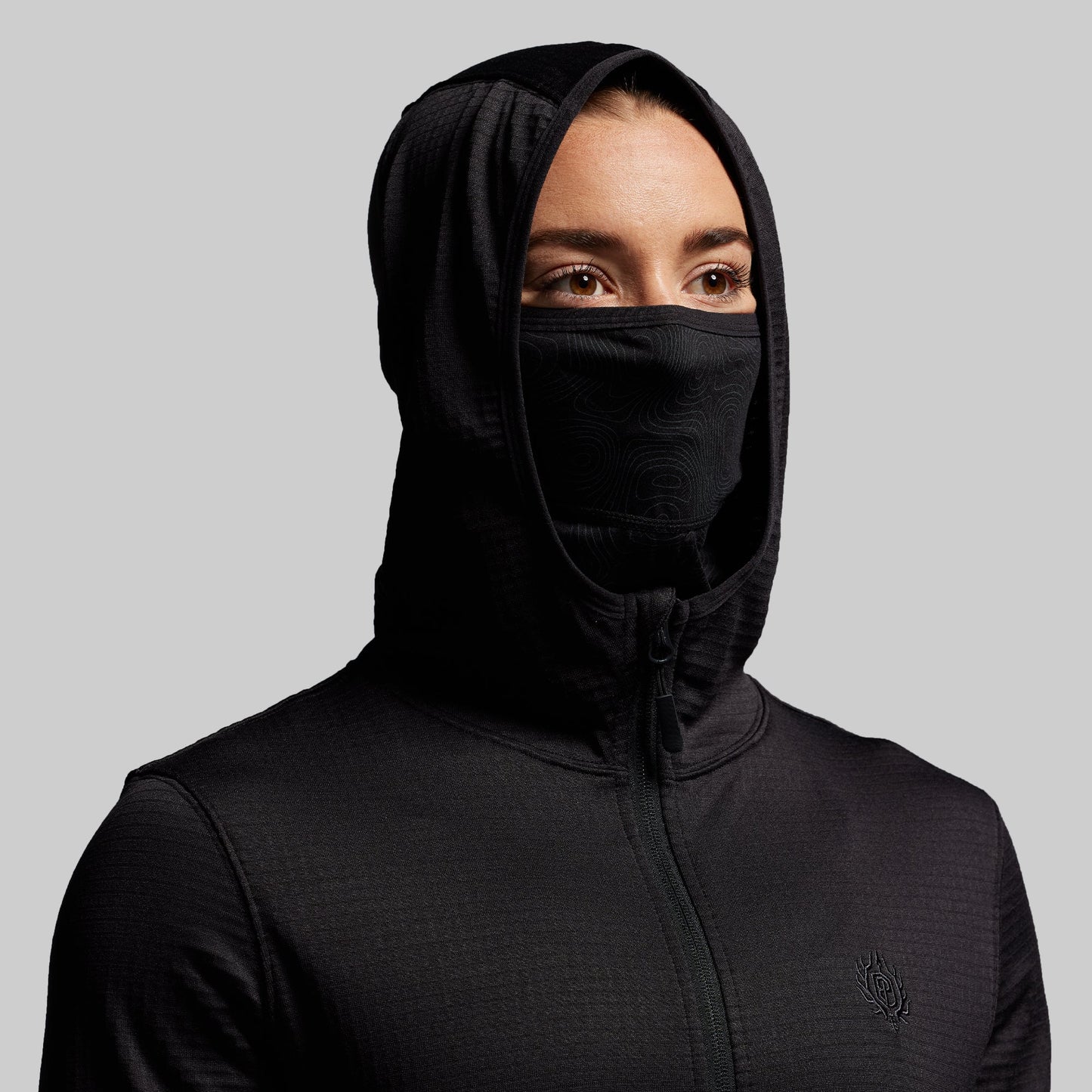 Person wearing a black hooded zip up with a face mask on a gray background
