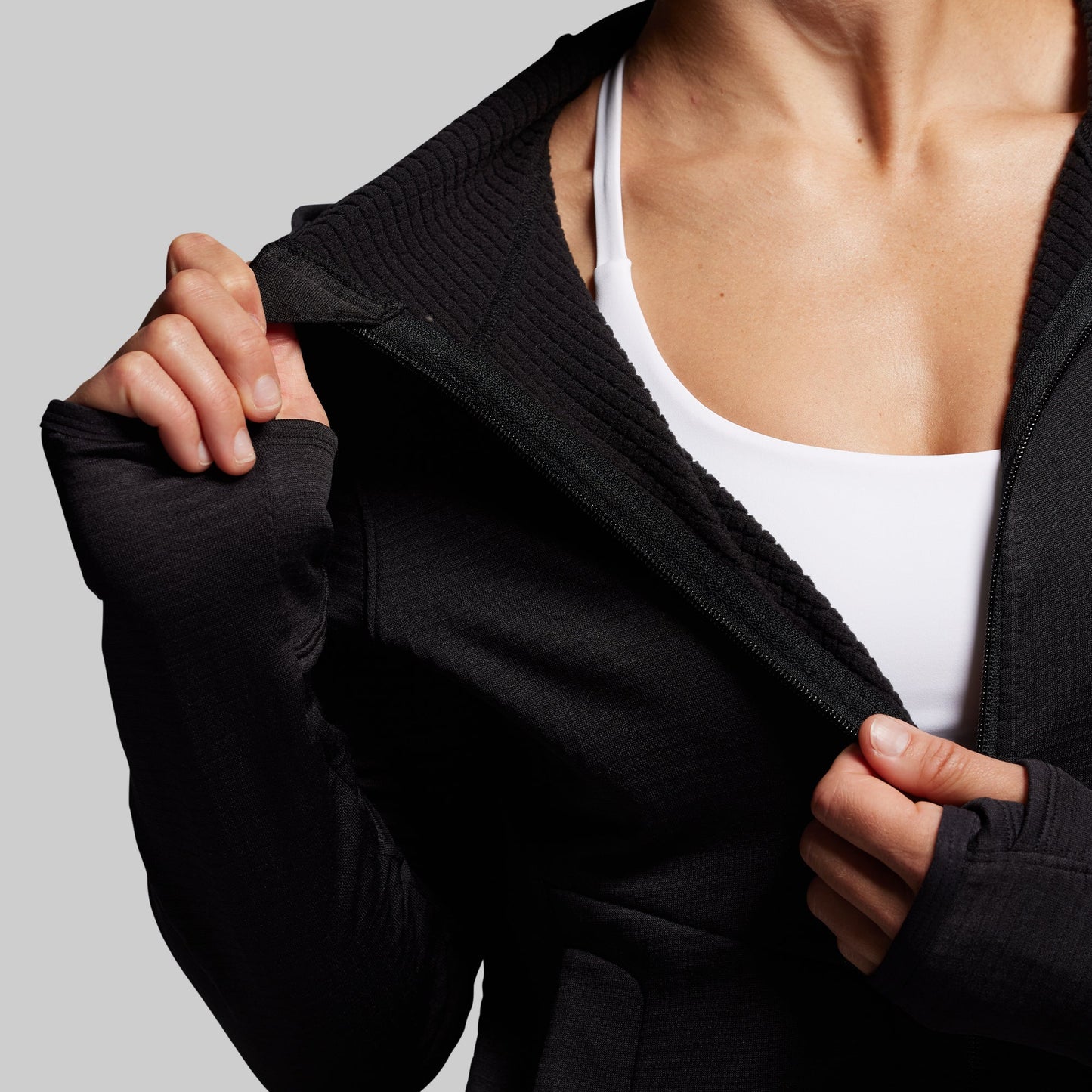 Person wearing a black full zip hoodie over a white top on a gray background