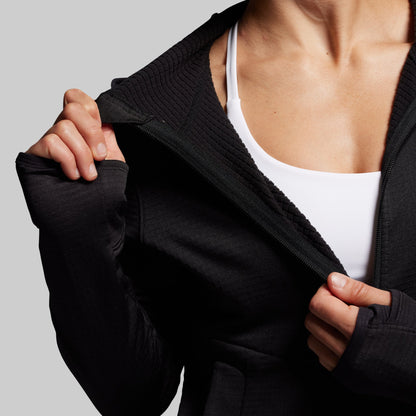 Person wearing a black full zip hoodie over a white top on a gray background