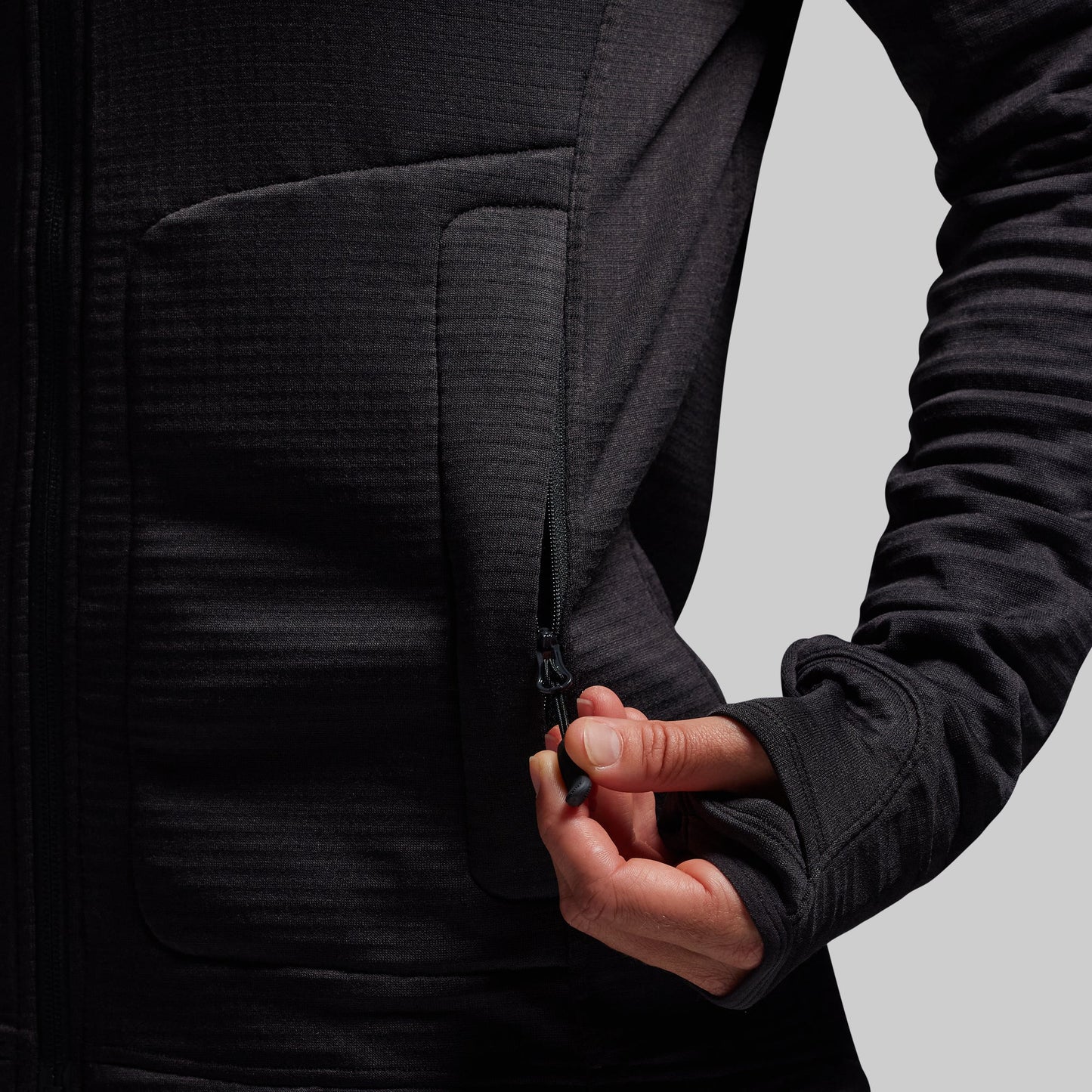 Person wearing a black hoodie with a focus on the zipper pocket.