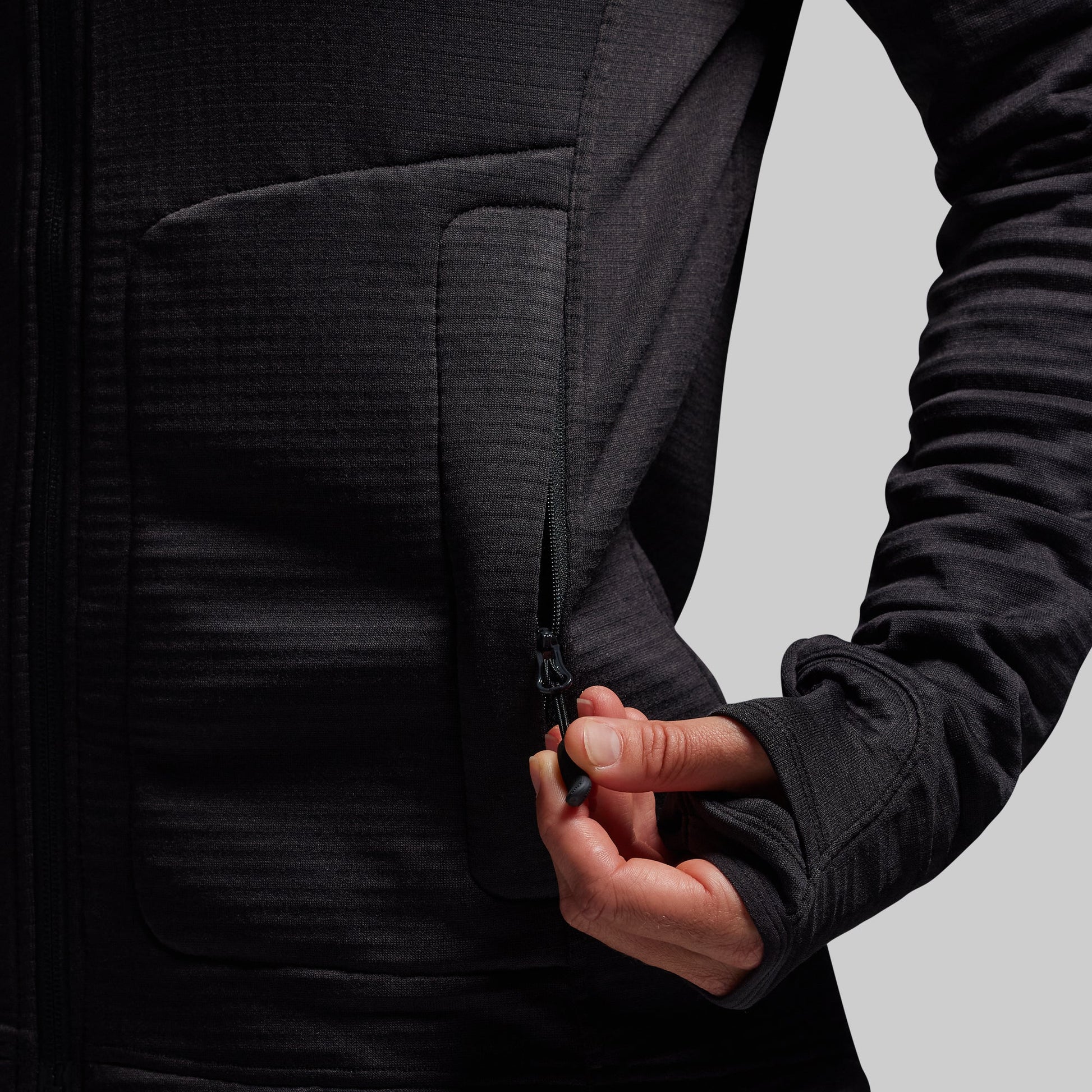 Person wearing a black hoodie with a focus on the zipper pocket.