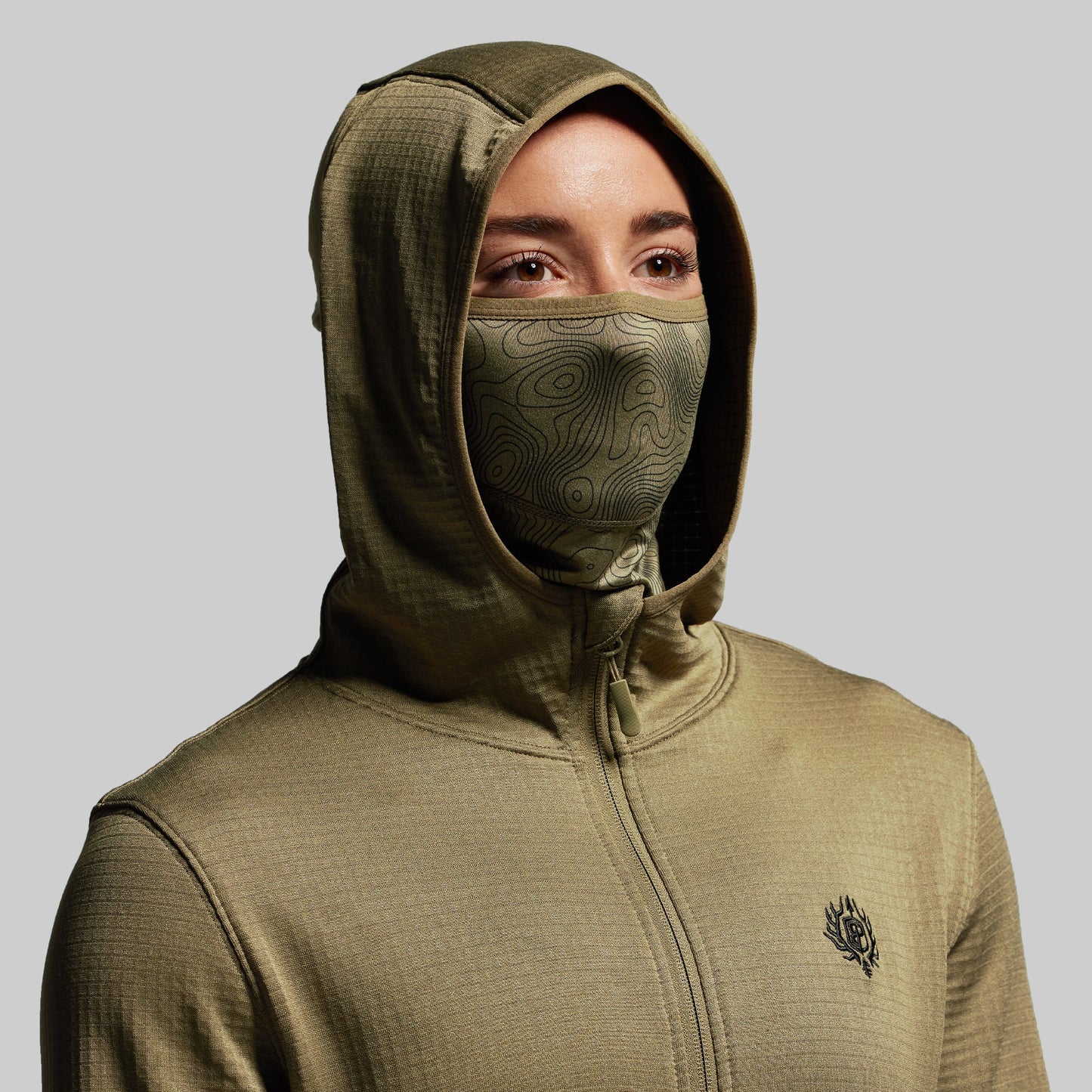 Person wearing a green hoodie with a built in face mask on a gray background