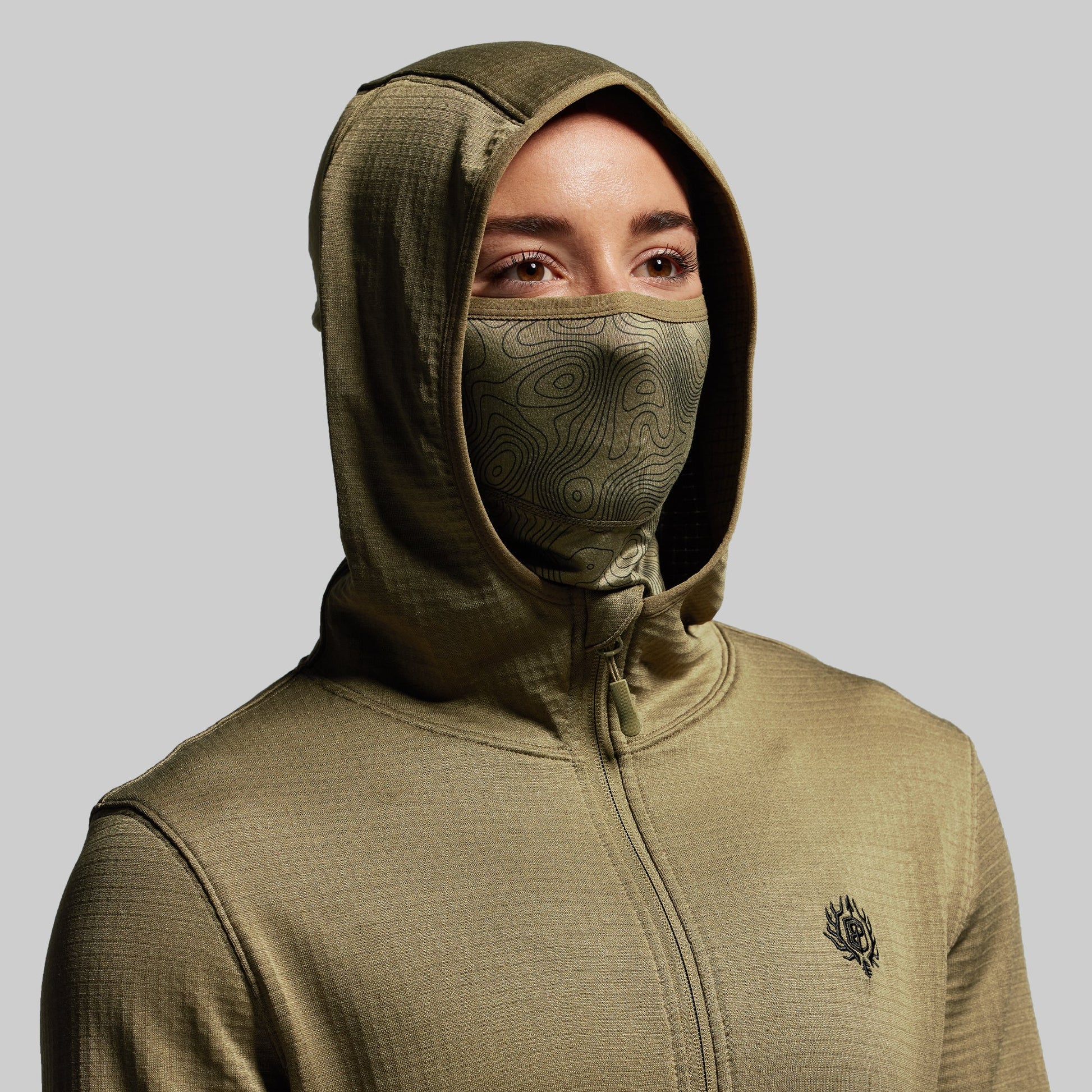 Person wearing a green hoodie with a built in face mask on a gray background