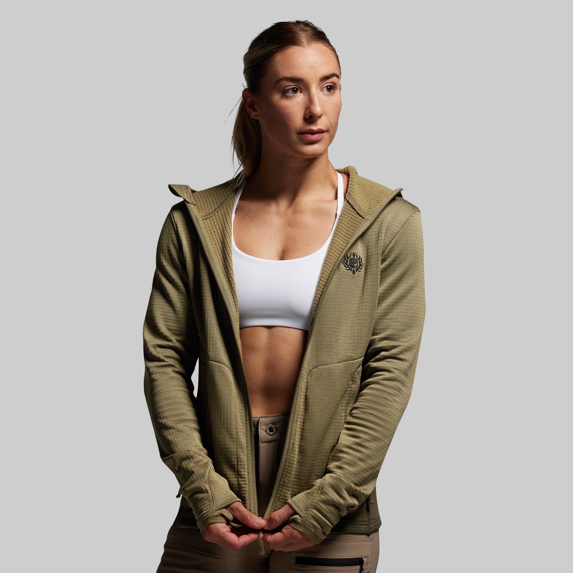 Woman wearing a green hoodie over a white sports bra on a gray background