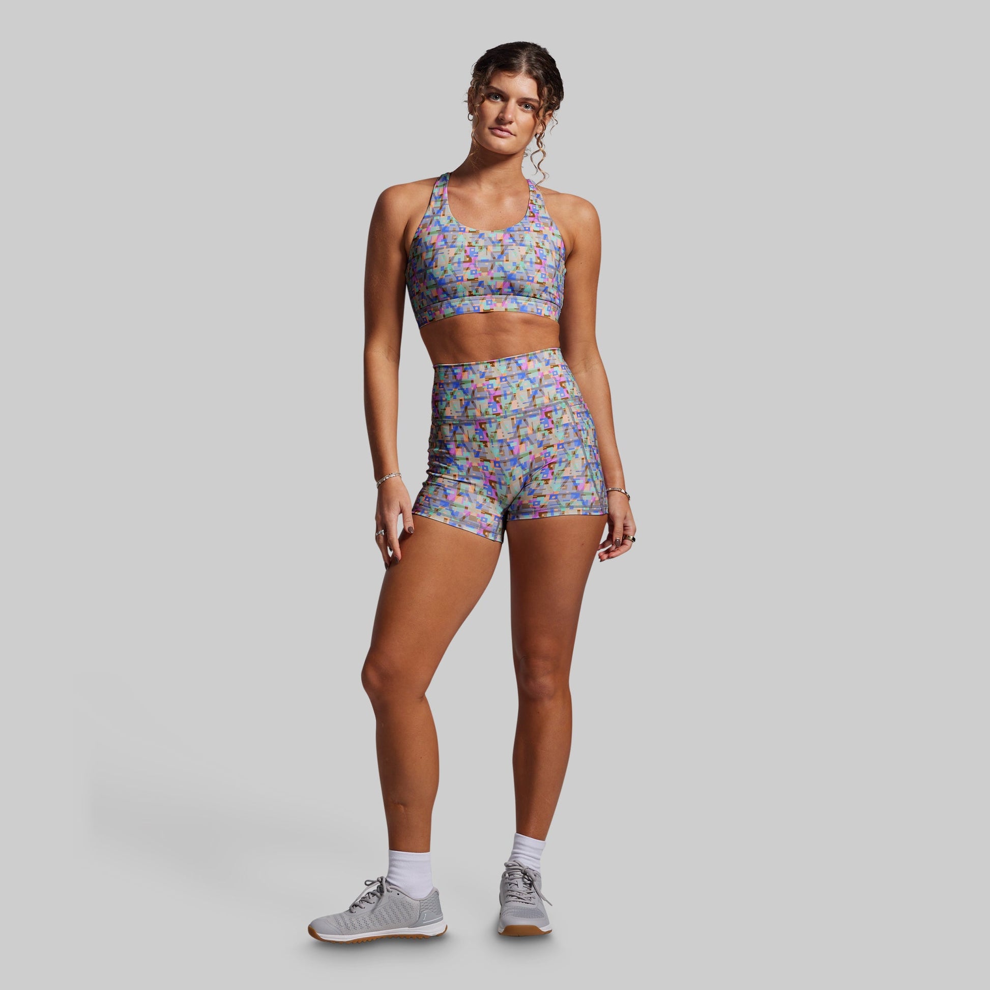 Woman wearing a colorful sports bra and shorts set on a gray background