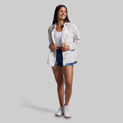Woman wearing a white plaid shirt, white tank top, blue shorts, and white sneakers on a gray background