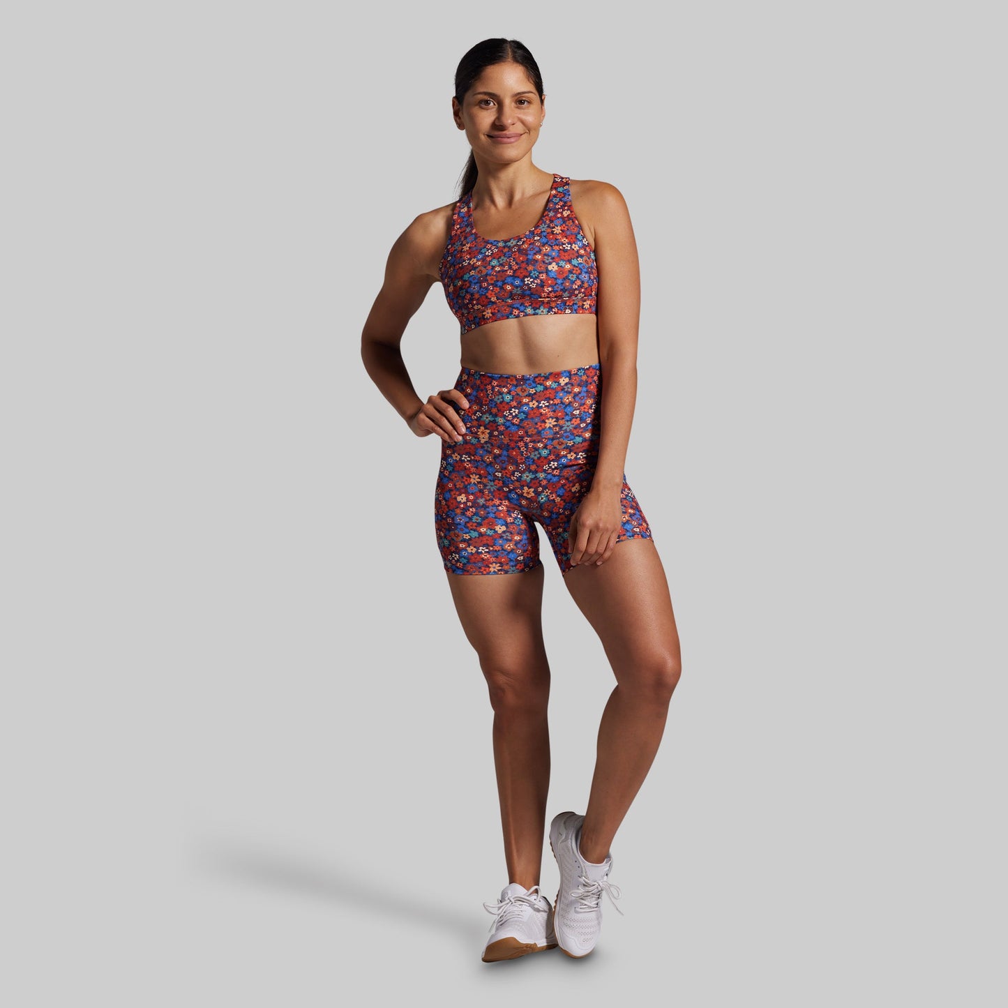 Woman wearing a colorful sports bra and shorts set on a gray background