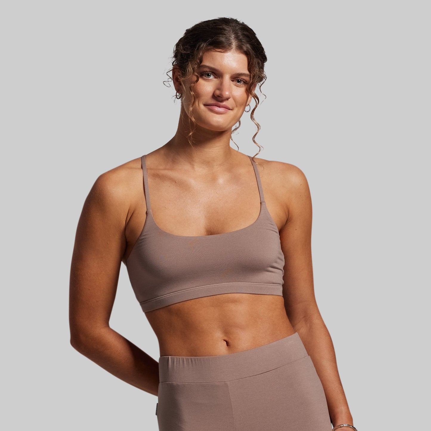 Woman wearing a brown sports bra and leggings against a gray background