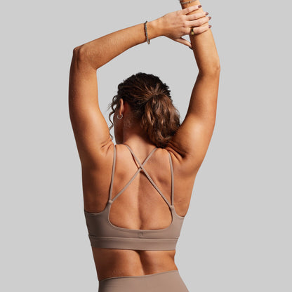 Woman wearing a beige sports bra and leggings with a plain background