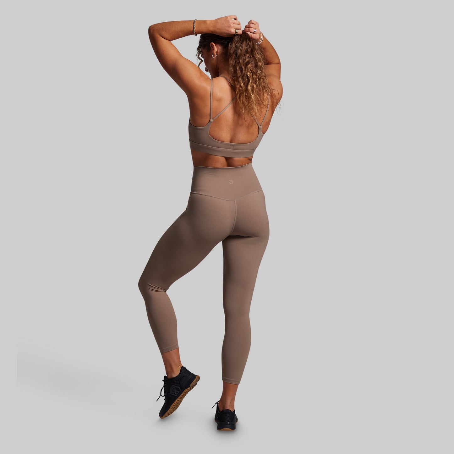 Woman wearing a brown sports bra and leggings on a gray background