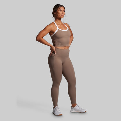 Woman wearing a brown sports bra and leggings set on a gray background