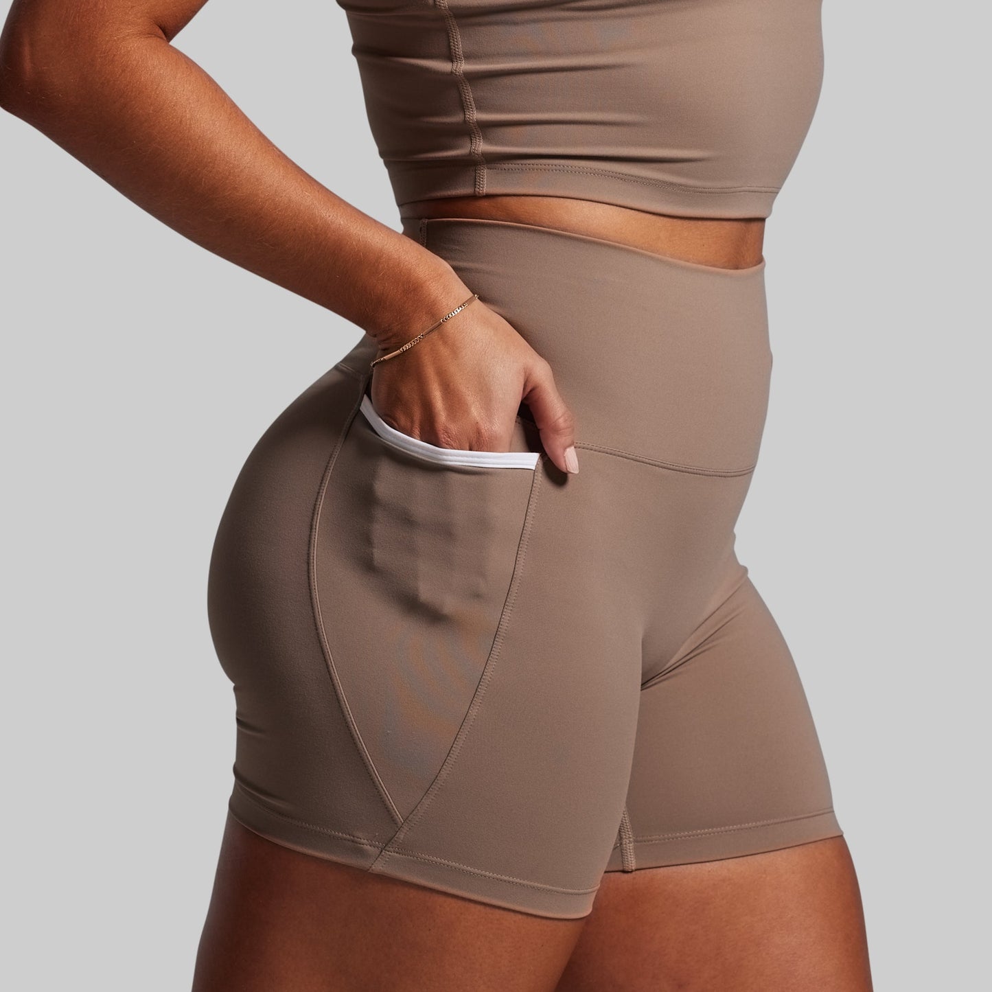 Person wearing brown athletic shorts and top on a light gray background