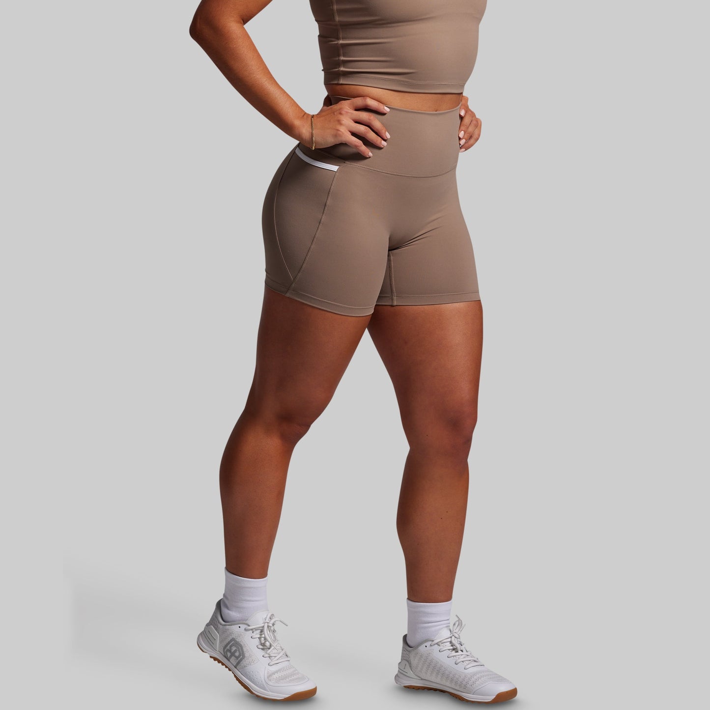 Person wearing brown athletic shorts and a matching sports bra on a gray background