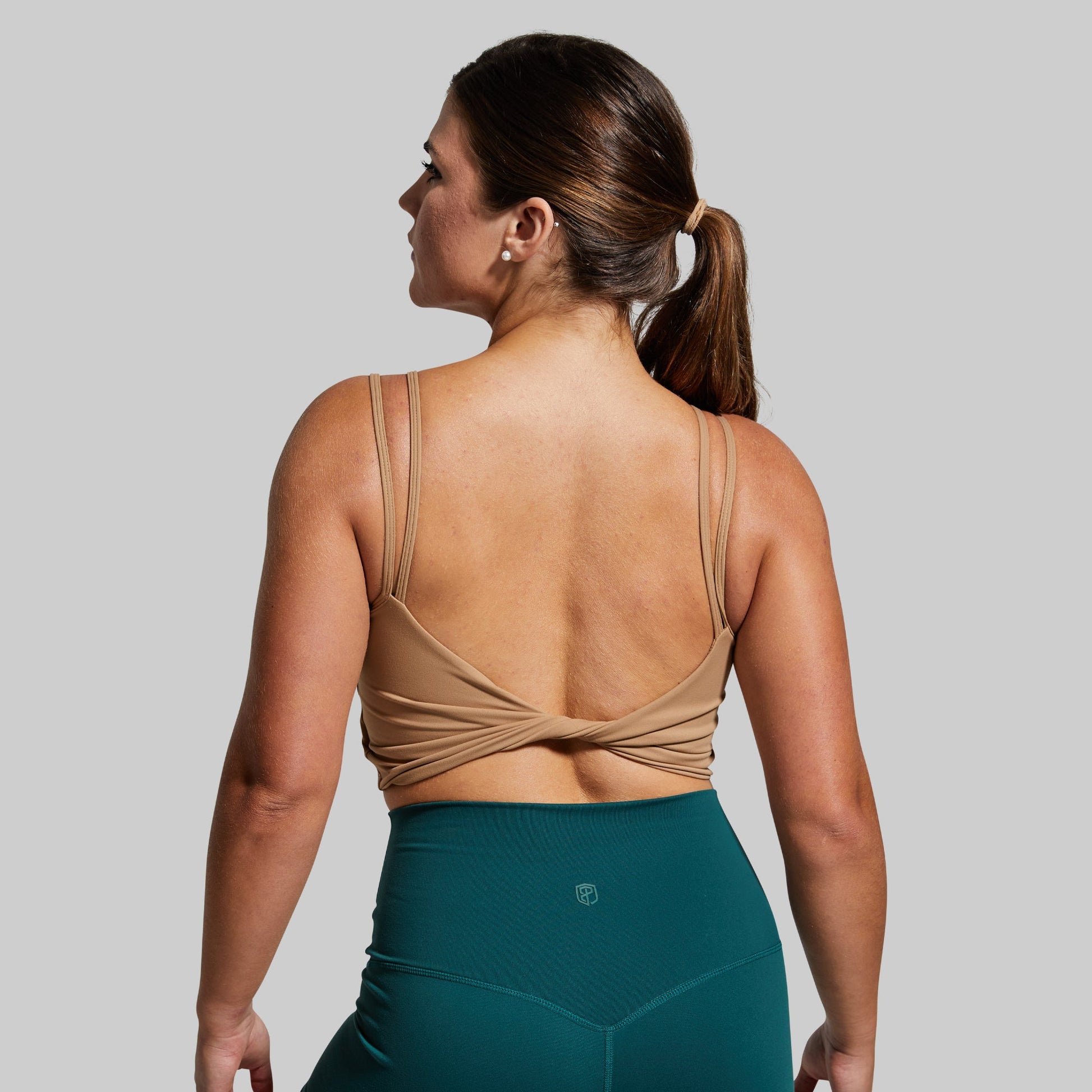 Woman wearing a beige sports bra and teal leggings on a gray background