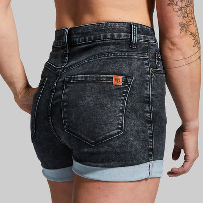 Person wearing black denim shorts with a visible brand logo on a gray background