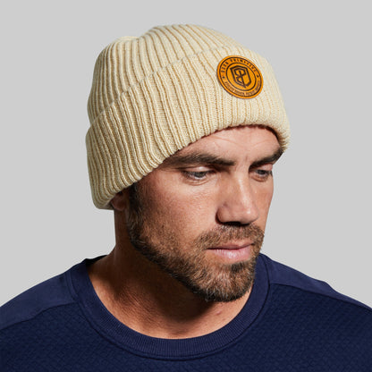 Man wearing a beige beanie with a logo on a gray background