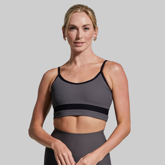 Woman wearing a gray sports bra and leggings against a plain background