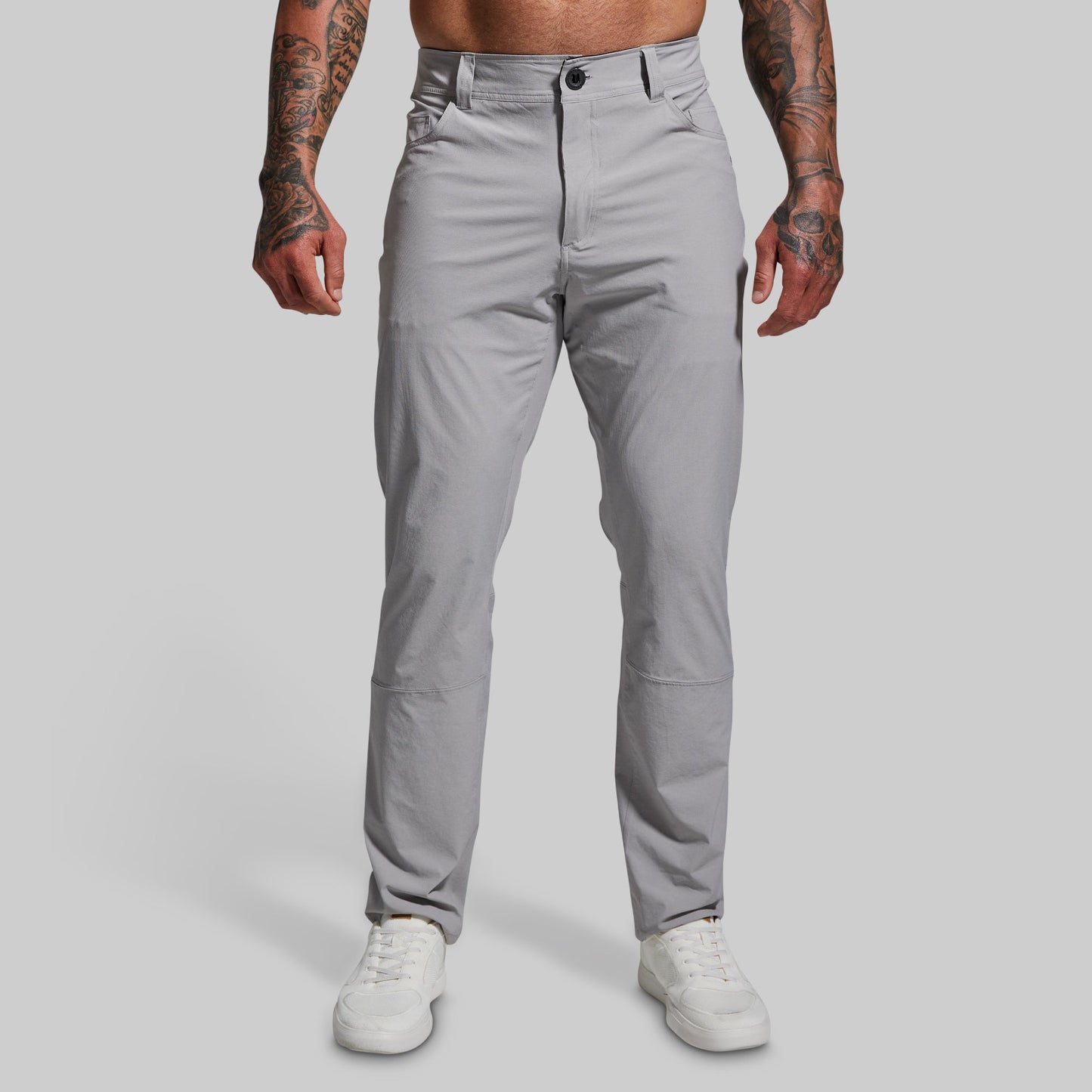 A male model wearing a pair of gray Traverse Pants with a button-and-fly closure, front pockets, and a regular fit.