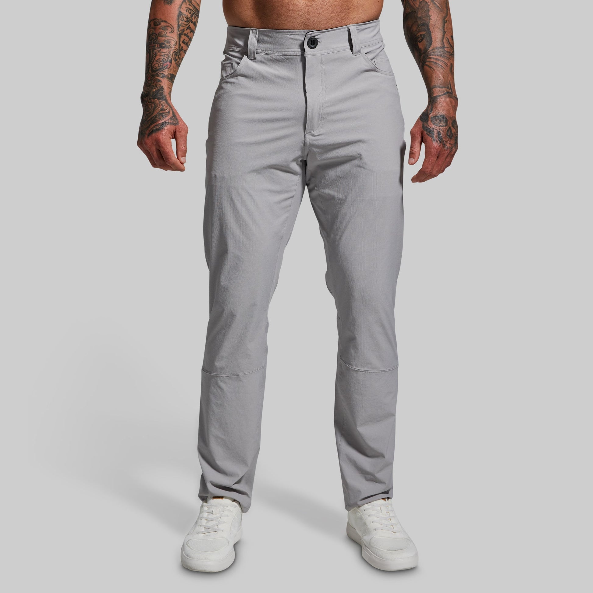 A male model wearing a pair of gray Traverse Pants with a button-and-fly closure, front pockets, and a regular fit.