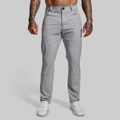 A male model wearing a pair of gray Traverse Pants with a button-and-fly closure, front pockets, and a regular fit.