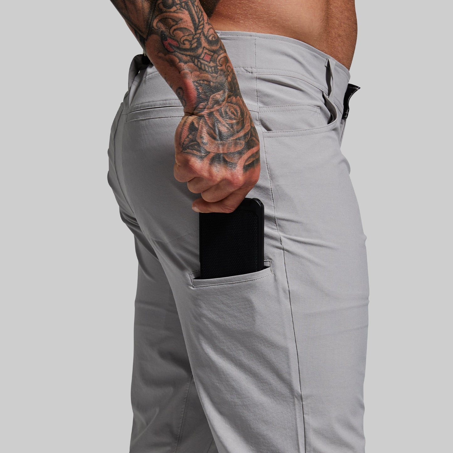 Close-up of man pulling a cell phone out of a side pocket on light gray pants.