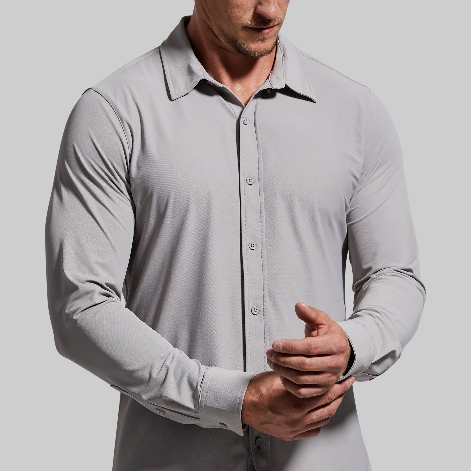 Close-up of a man wearing a light gray button-up shirt adjusting sleeve cuff.