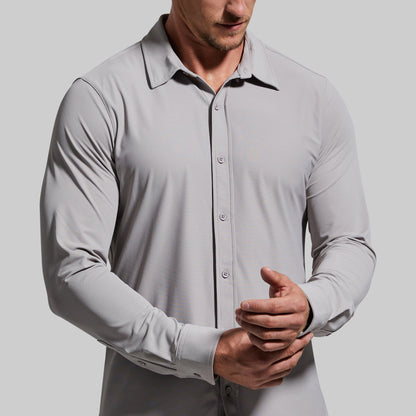 Close-up of a man wearing a light gray button-up shirt adjusting sleeve cuff.