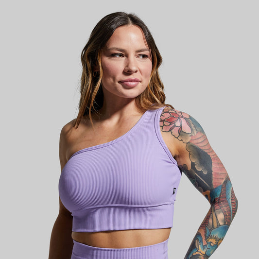 Woman wearing a purple one-shoulder sports bra against a plain background