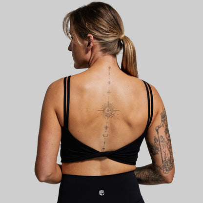 Woman wearing a black sports bra with visible tattoos on a plain 