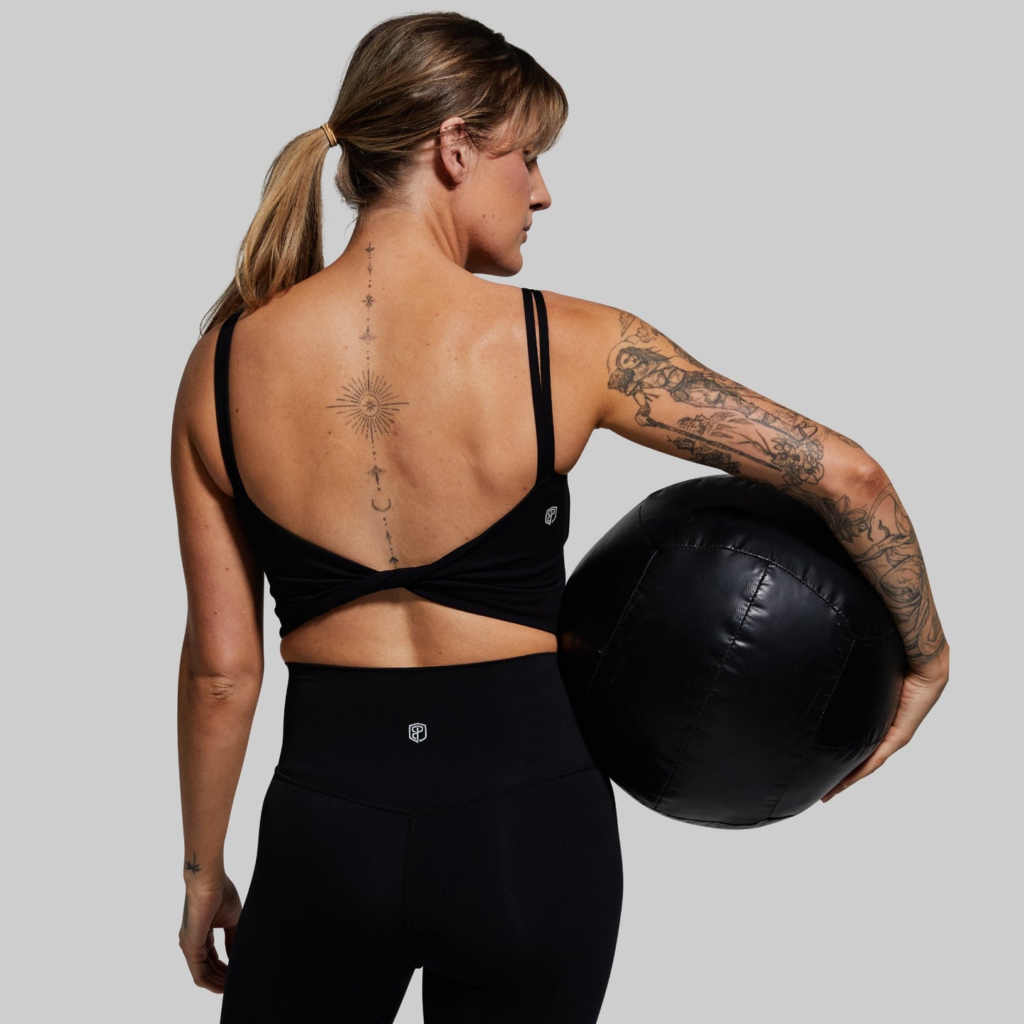 Woman wearing a black sports bra holding a medicine ball on a plain background