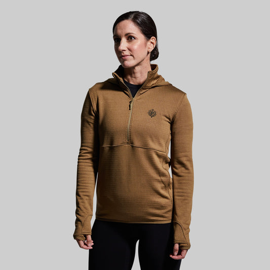 A woman wearing a coyote brown half zip hoodie with a hood, paired with black pants.