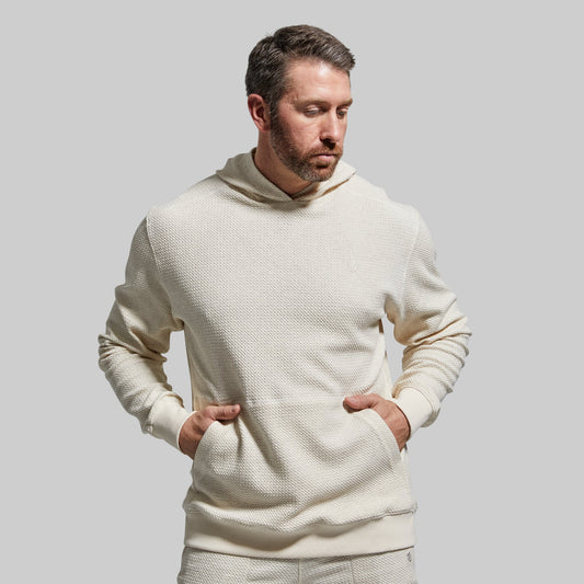 A man wearing a beige hooded sweatshirt with a waffle-textured material.
