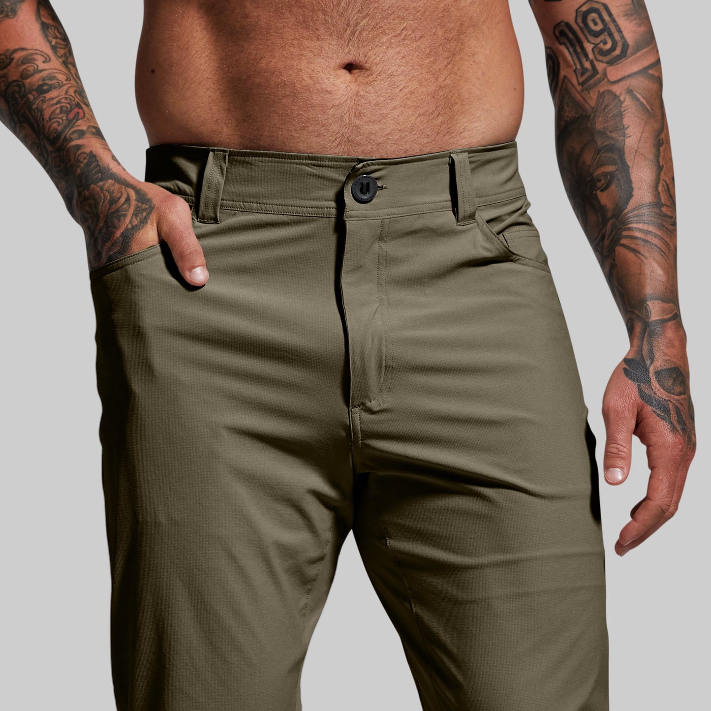 Close-up of a waistband with button-and-fly closure and belt loops on pair of green pants worn by a person.
