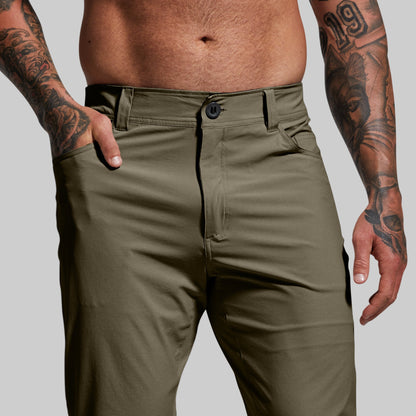 Close-up of a waistband with button-and-fly closure and belt loops on pair of green pants worn by a person.