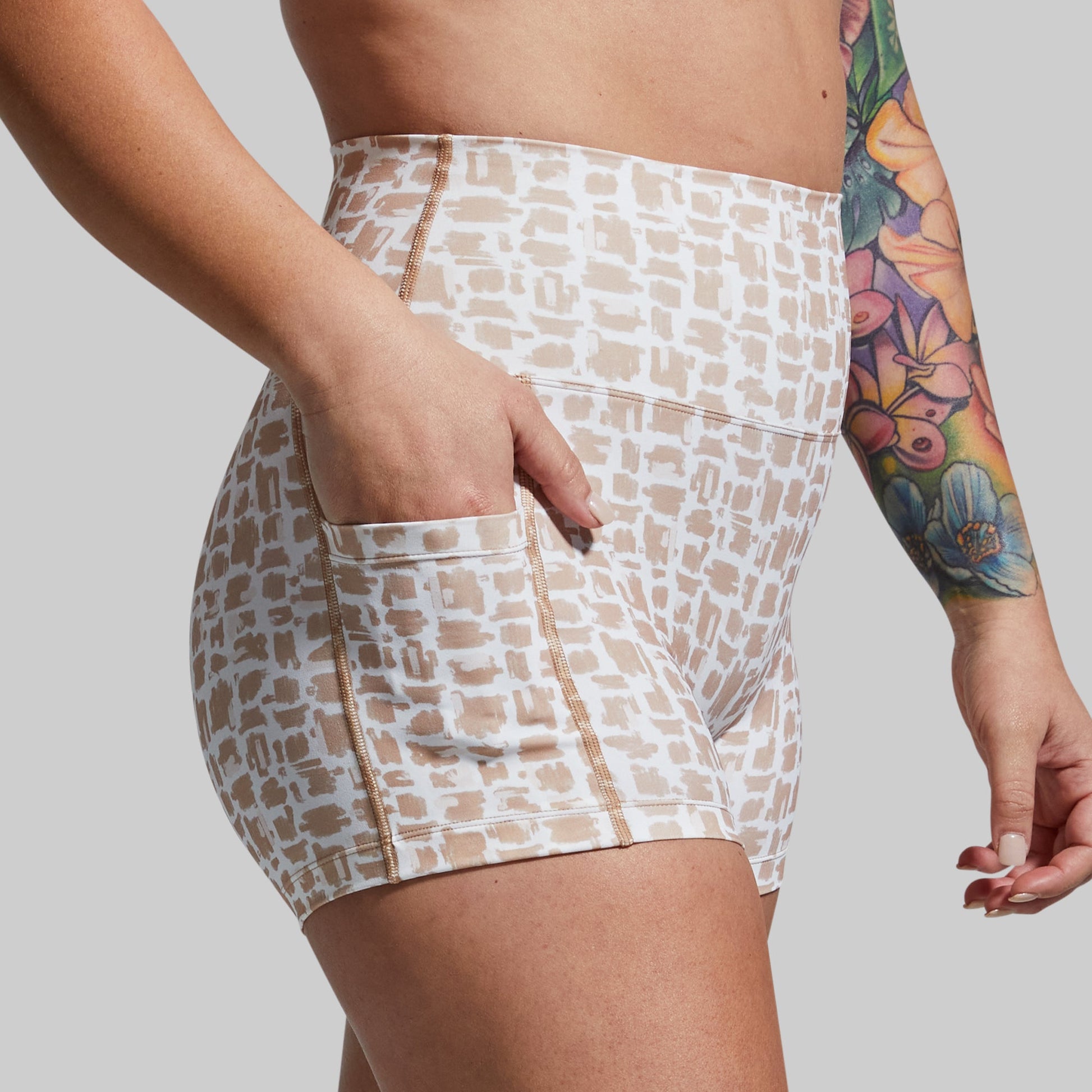 Person wearing patterned shorts with a tattooed arm on a plain background