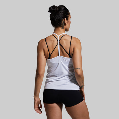 Woman wearing a white tank top with racerback design and black shorts on a gray background