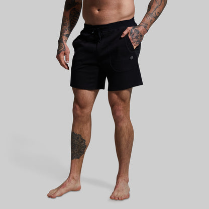 A male model wearing black lounge shorts with a textured surface, standing against a plain background.