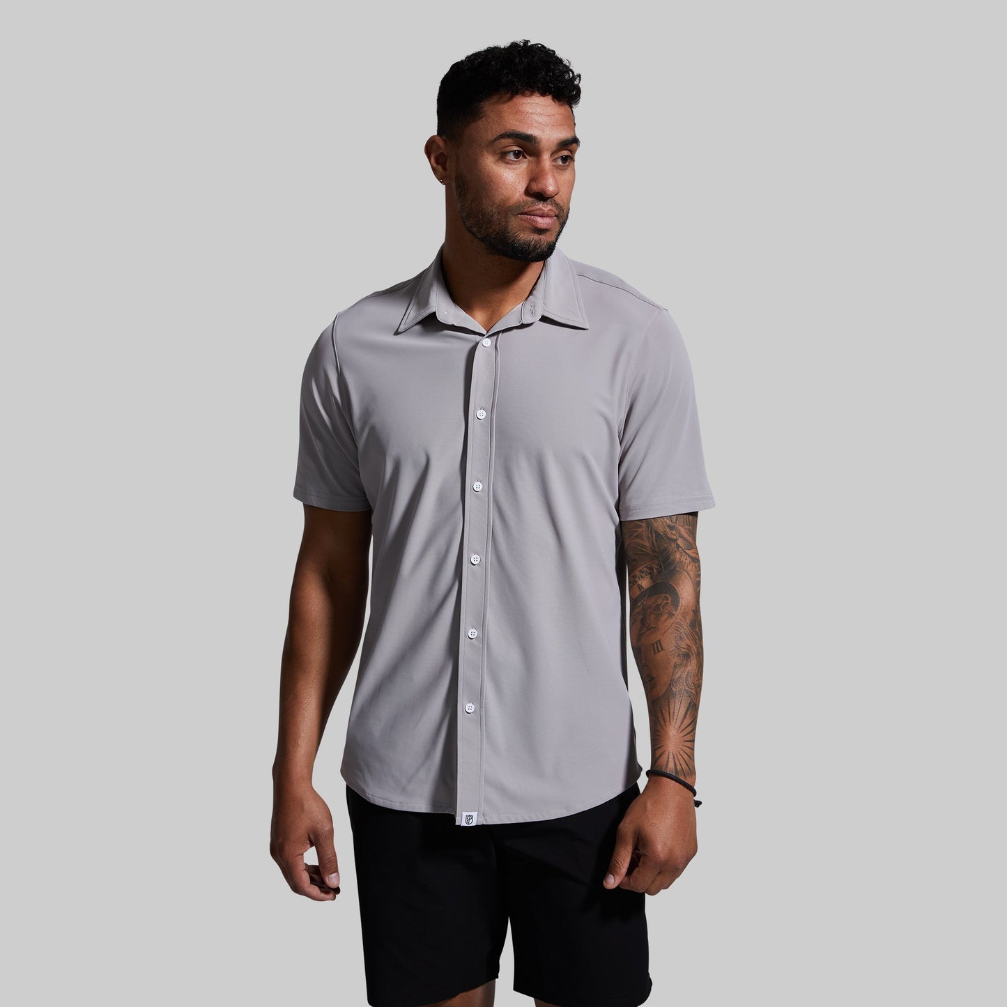 A man wearing a short sleeve button-down shirt in gray color, paired with black shorts.