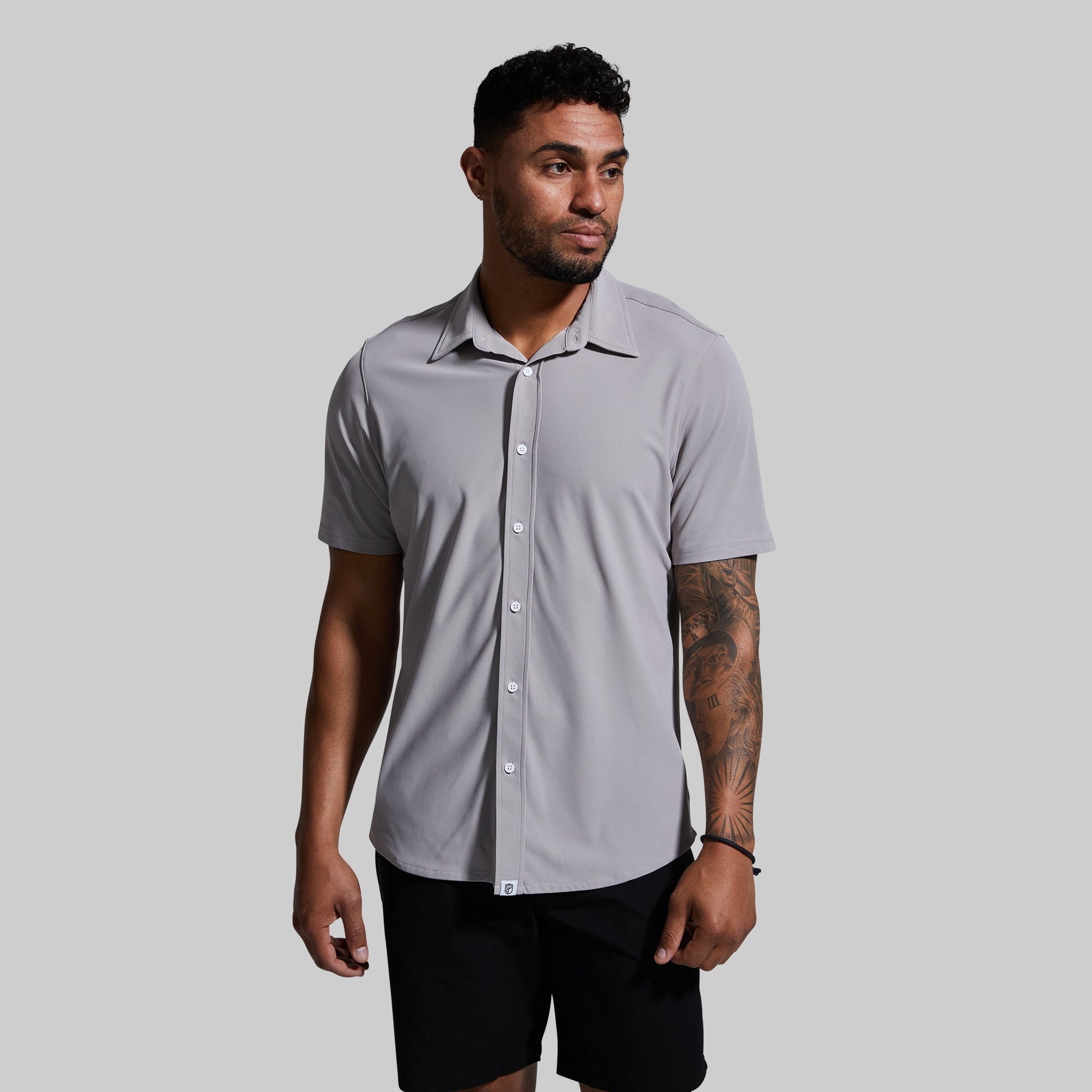 A man wearing a short sleeve button-down shirt in gray color, paired with black shorts.