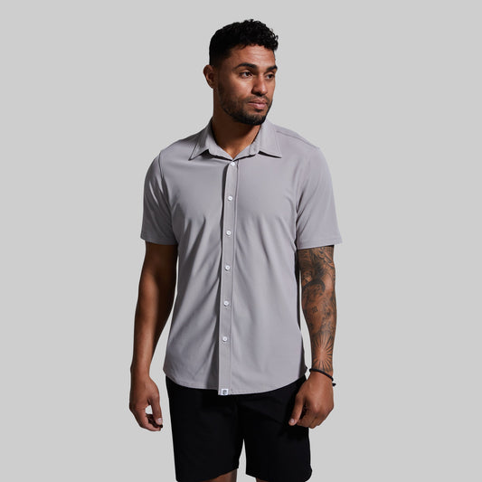 A man wearing a short sleeve button-down shirt in gray color, paired with black shorts.